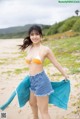 A woman in a bikini top and denim shorts on a beach.